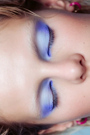 Close-up portrait of a woman with closed eyes featuring gradient blue eye makeup and light brows by Shella Ruby Martin