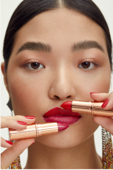 Close-up of a fair-skinned adult female with two shades of lipstick near her lips in an indoor beauty studio setting.