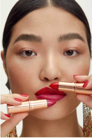 Close-up of a fair-skinned adult female with two shades of lipstick near her lips in an indoor beauty studio setting.
