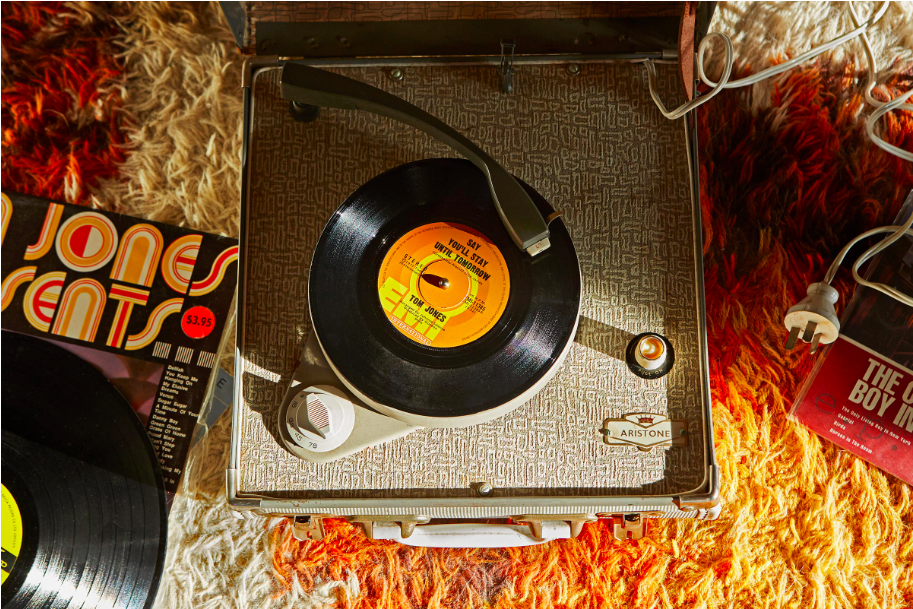 Vintage record player with vinyl record on shag carpet, with album covers. Warm, nostalgic vibe.