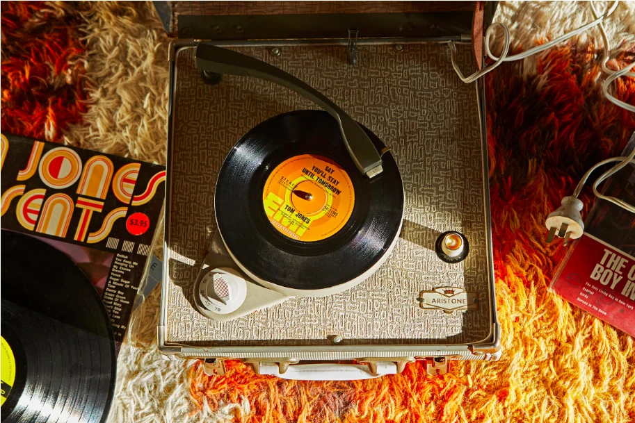 Vintage record player with vinyl record on shag carpet, with album covers. Warm, nostalgic vibe.