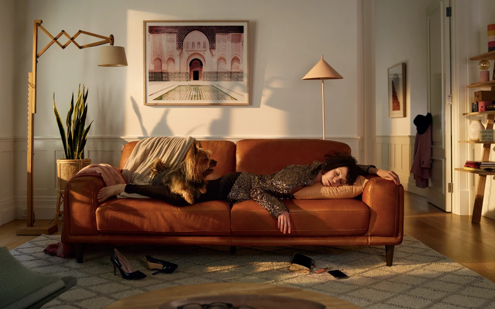 Woman resting on a leather sofa with a small dog, photographed by Heather Dinas in a sunlit living room.