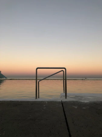 Still water in a concrete pool at dusk with metal railings and a soft color gradient in the sky from light blue to orange.