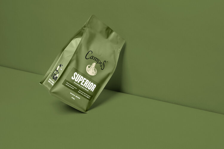 Two green Campos coffee bags with a minimalist design are positioned against a matching green backdrop, highlighting the packaging.