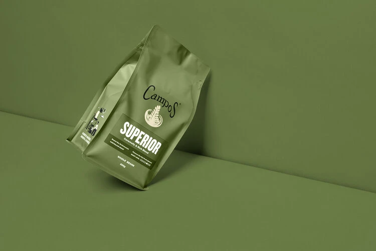 Two green Campos coffee bags with a minimalist design are positioned against a matching green backdrop, highlighting the packaging.