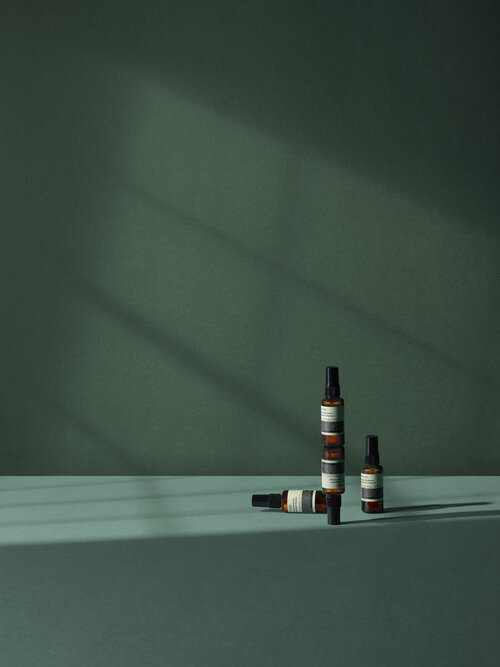 Still life shot of three amber-colored bottles with spray nozzles displayed against an emerald green backdrop in a minimalist composition.