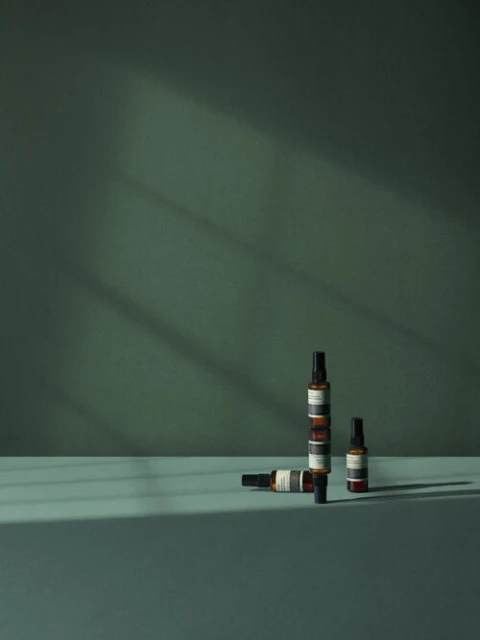 Still life shot of three amber-colored bottles with spray nozzles displayed against an emerald green backdrop in a minimalist composition.