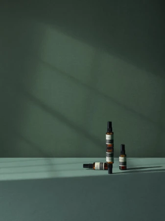 Still life shot of three amber-colored bottles with spray nozzles displayed against an emerald green backdrop in a minimalist composition.