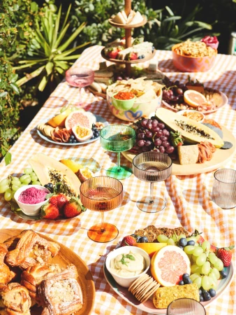 A cheerful outdoor picnic setting with colorful drinks, fresh fruit, gourmet snacks, and checkered tablecloth on a sunny day.