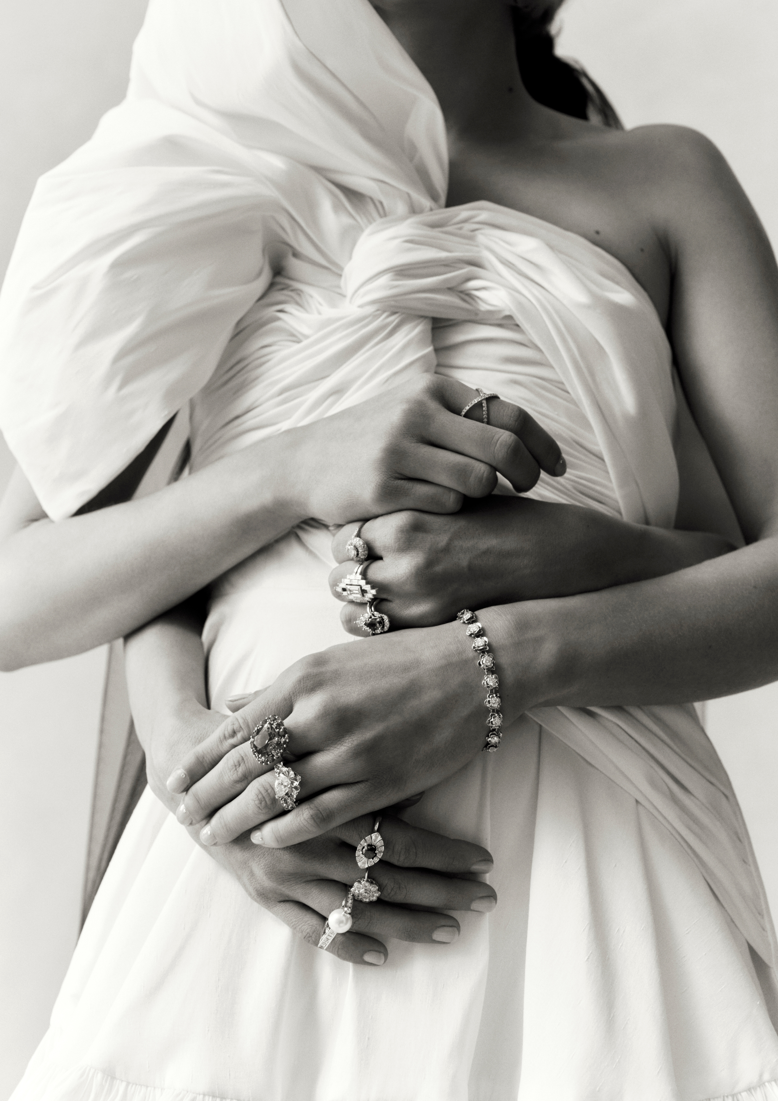 Close-up studio shot of two adult women's arms and hands adorned with various rings and a bracelet, showcasing fashion and jewelry.
