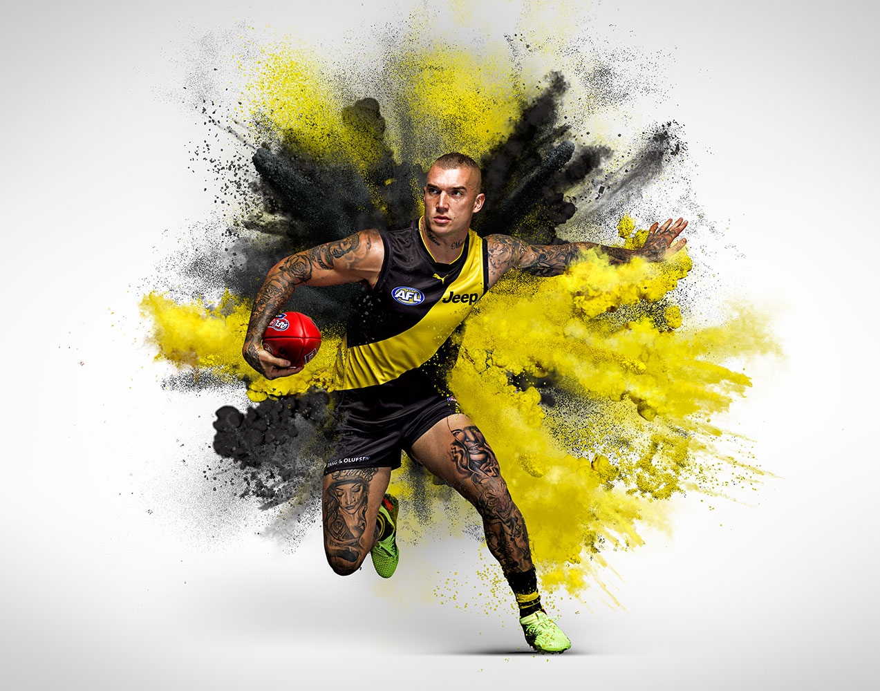 Action shot of a muscular adult male athlete running with a football amidst a burst of black and yellow powder against a white backdrop.