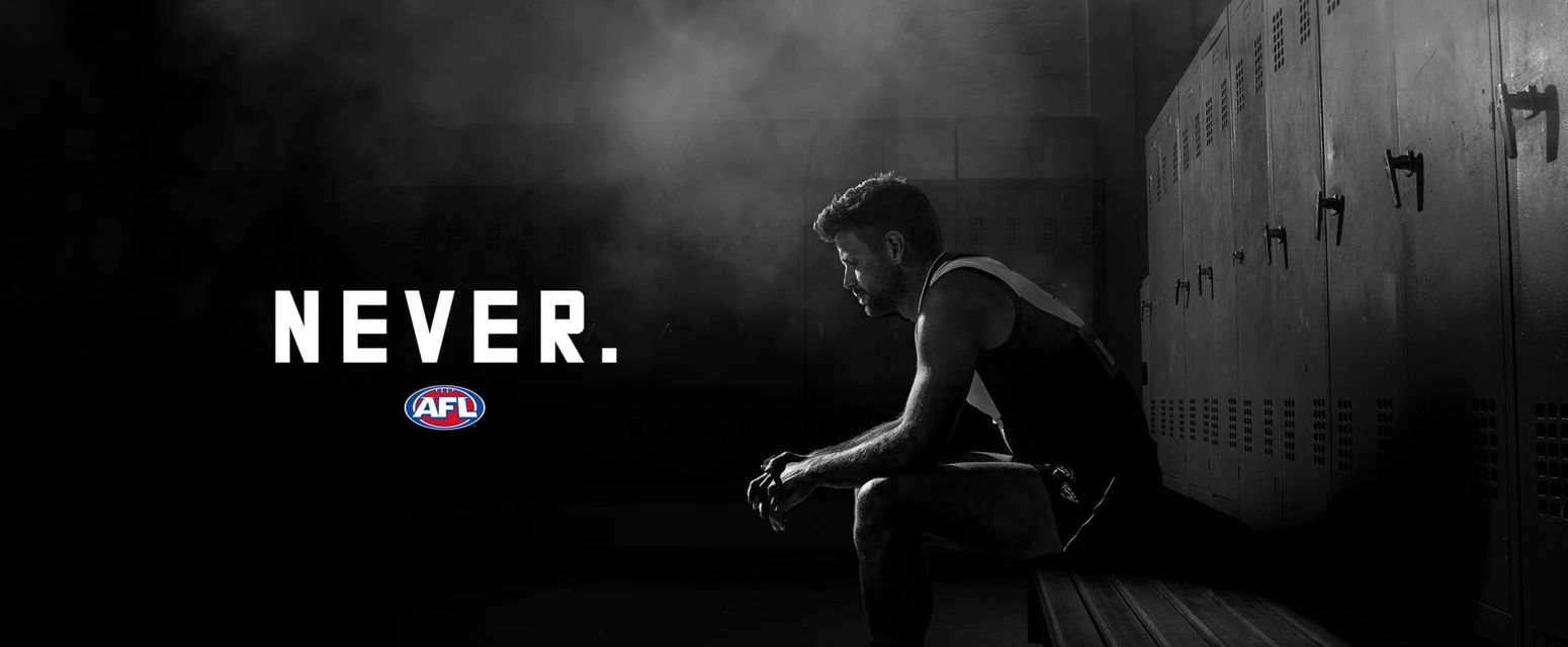 Monochrome image of a male athlete in a locker room sitting on a bench, with the text 'NEVER.' and the AFL logo visible.