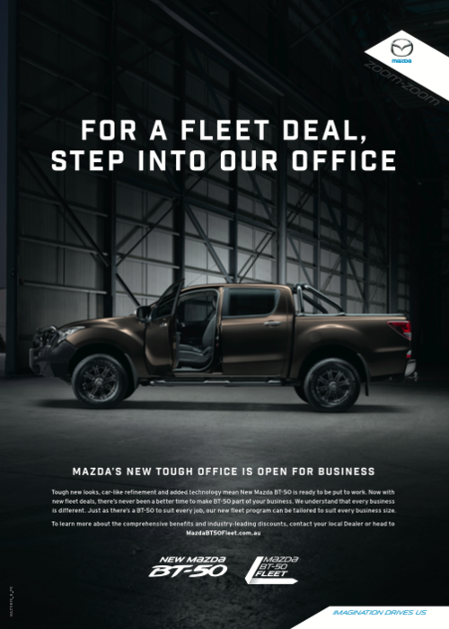 Brown Mazda BT-50 pickup truck parked inside a warehouse-style building, spotlighted with an open driver door.