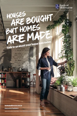 Woman stands near a window with many houseplants in an apartment with natural lighting, brick walls, and wood floors; home loan ad.