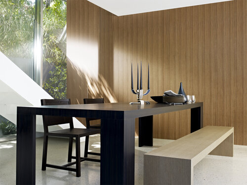 Modern dining room interior with wood paneled walls, contemporary table and chairs, bench, and view to outdoor greenery through a large window.
