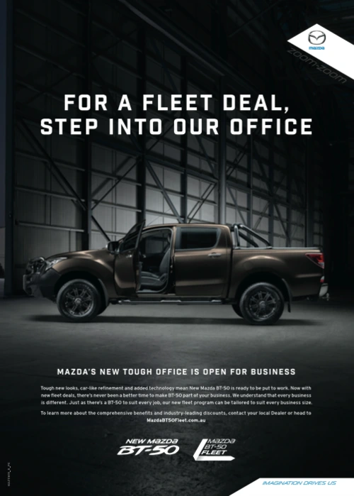 Brown pickup truck parked inside a large industrial warehouse with prominent structural girders and bold advertising text overhead.