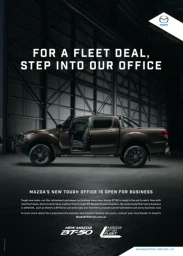 Brown pickup truck parked inside a large industrial warehouse with prominent structural girders and bold advertising text overhead.