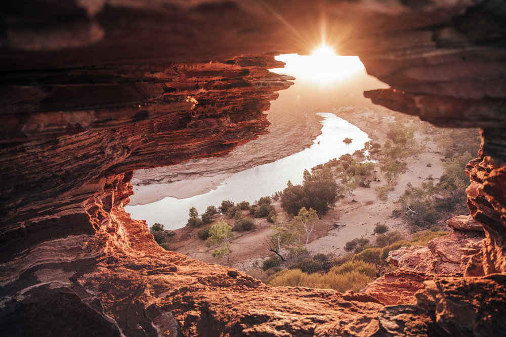 Scenic landscape of a river through the sandstone cliffs and rock formations, with a bright sunburst shining through the opening.