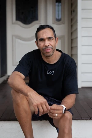 Portrait of an Indigenous man in a black t-shirt seated on wooden porch steps by Charlie Kinross