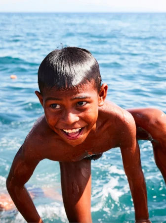 Young boy smiling with wet hair in the sea against a backdrop of blue ocean water photographed by James Geer.