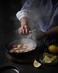 Chef cooking sliced sausages in a cast iron pan with rising steam, photographed by Brent Parker Jones.