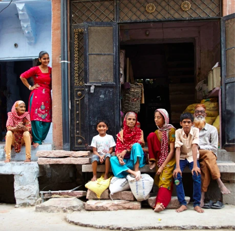 Family group poses on steps outside a building in India, with women in traditional clothing and a smiling child. 