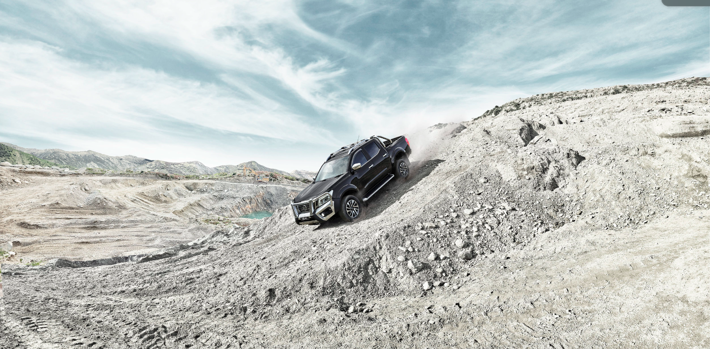 Black pickup truck driving on a rocky landscape against a cloudy sky, with a blue pond visible in the background. 