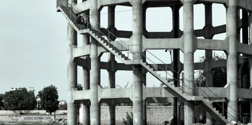 Monochrome architectural photograph of a large concrete water tower structure with an exterior staircase.