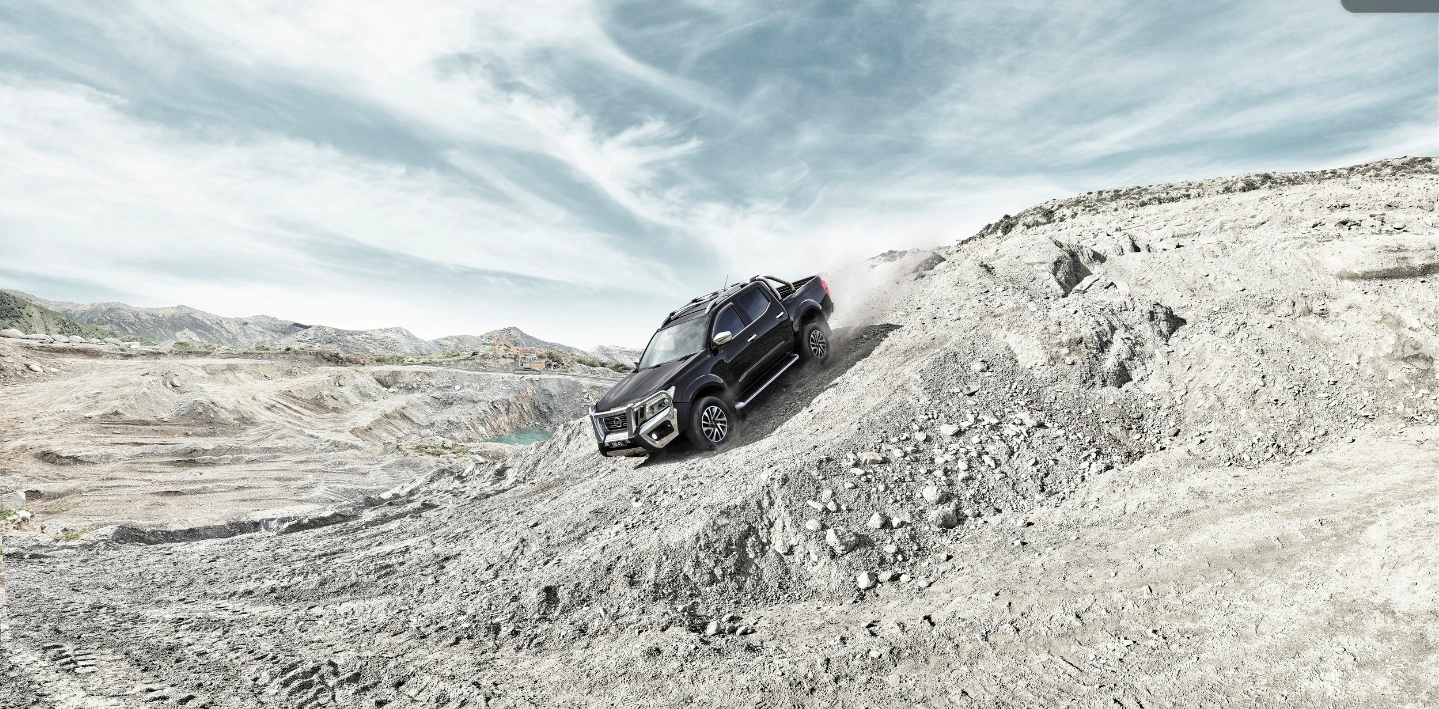 Black pickup truck descending a steep rocky dirt slope in a quarry under a pale overcast sky