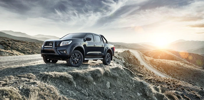 A black pickup truck parked on a rocky mountain ridge under a dramatic cloudy sky at sunset, photographed by Lou D'Angelo.