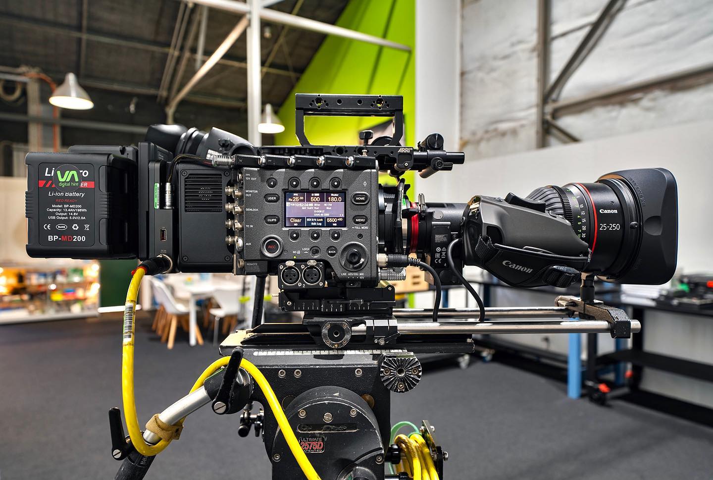 Professional digital cinema camera on a tripod in a studio setting. Includes a Canon lens and Livayo digital lithium-ion battery.