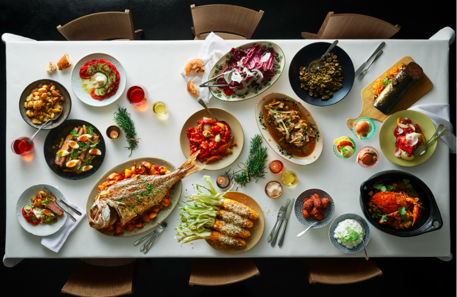Overhead shot of a beautifully arranged table filled with various dishes, including fish, salads, and vegetables, set for a feast.