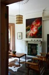 Interior view of a living room with wooden armchairs, a coffee table, a fireplace, and an abstract painting by Earl Carter