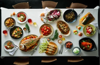 Overhead view of a long dining table laden with a feast of roasted fish, salads, corn, and various dishes photographed by Earl Carter.