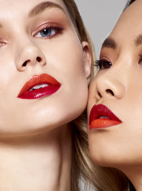 Close-up studio shot of two women with vibrant orange and red ombre lips and complementary makeup, showcasing beauty and fashion.