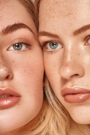 Close-up portrait of two young women with natural freckles and light grey eyes styled by Samantha Coles