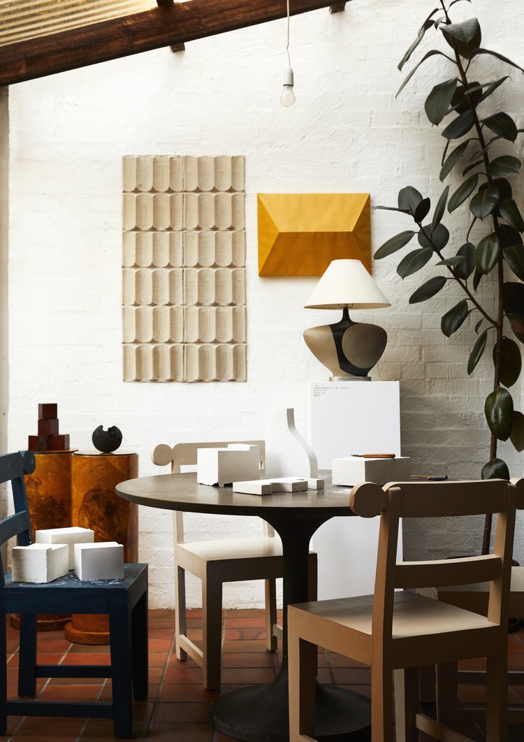 Interior design shot with round table, chairs, lamp, decorative objects, and white brick wall in a well-lit setting.