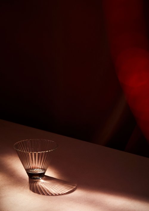 Fluted clear glass vase on a white surface with a dark background and red accents, creating a simple and elegant product shot.