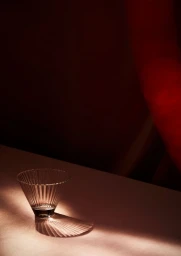 A clear fluted glass vessel sits on a flat surface casting a ribbed shadow under dramatic red lighting