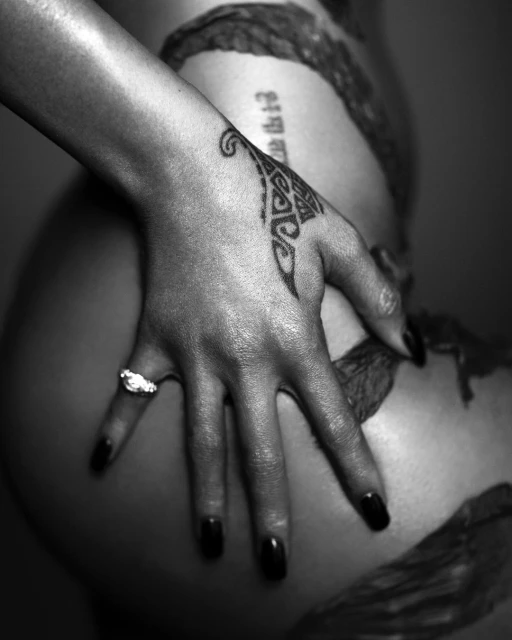 Black and white studio shot of a fair-skinned adult female hand with black nail polish, diamond ring and tattoo covering woman's body.