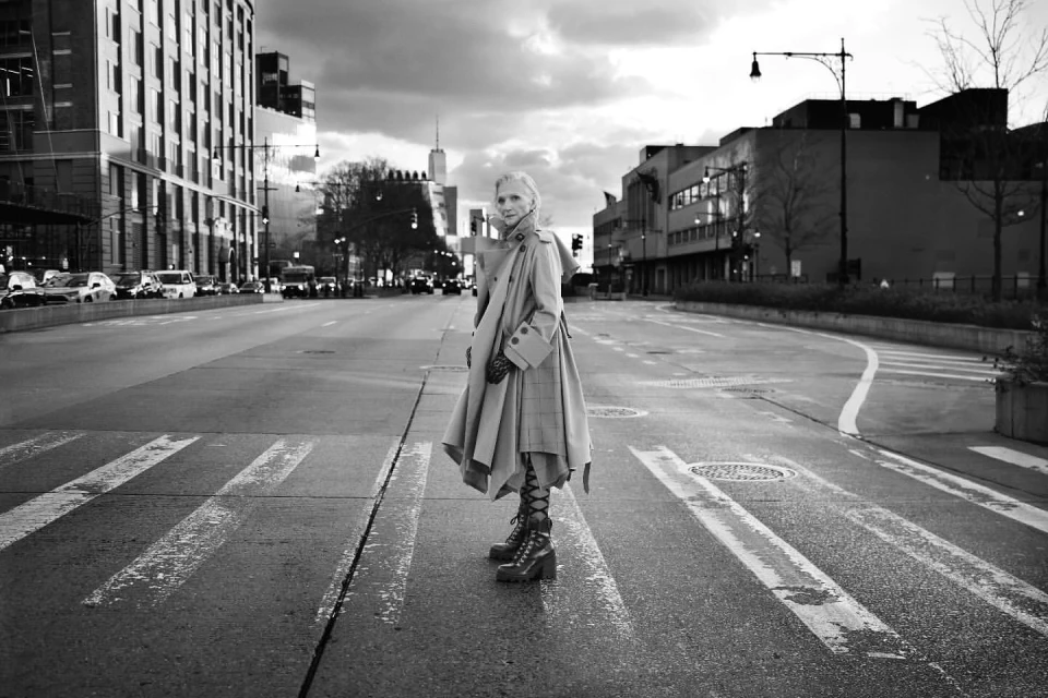 Monochrome portrait of an adult female in a stylish coat and boots crossing an urban street in a city setting.