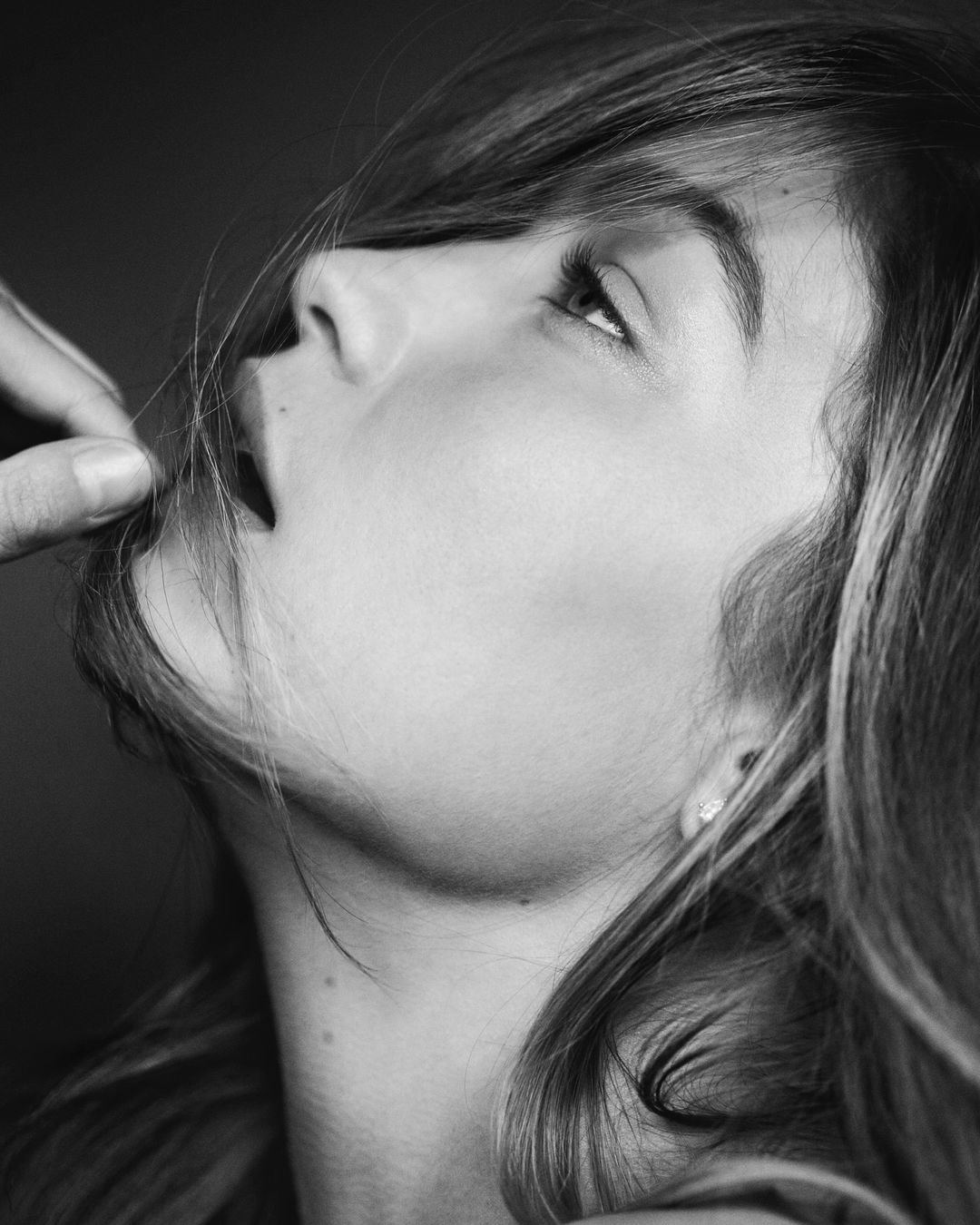 Close-up black and white portrait of a woman looking upward while a hand gently touches her hair by Russell James.