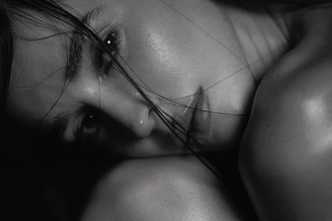 Close-up black and white portrait of a woman resting her head, with strands of hair falling across her face.