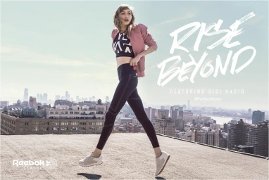 Gigi Hadid wearing athletic apparel while jumping on a city rooftop against a distant skyline