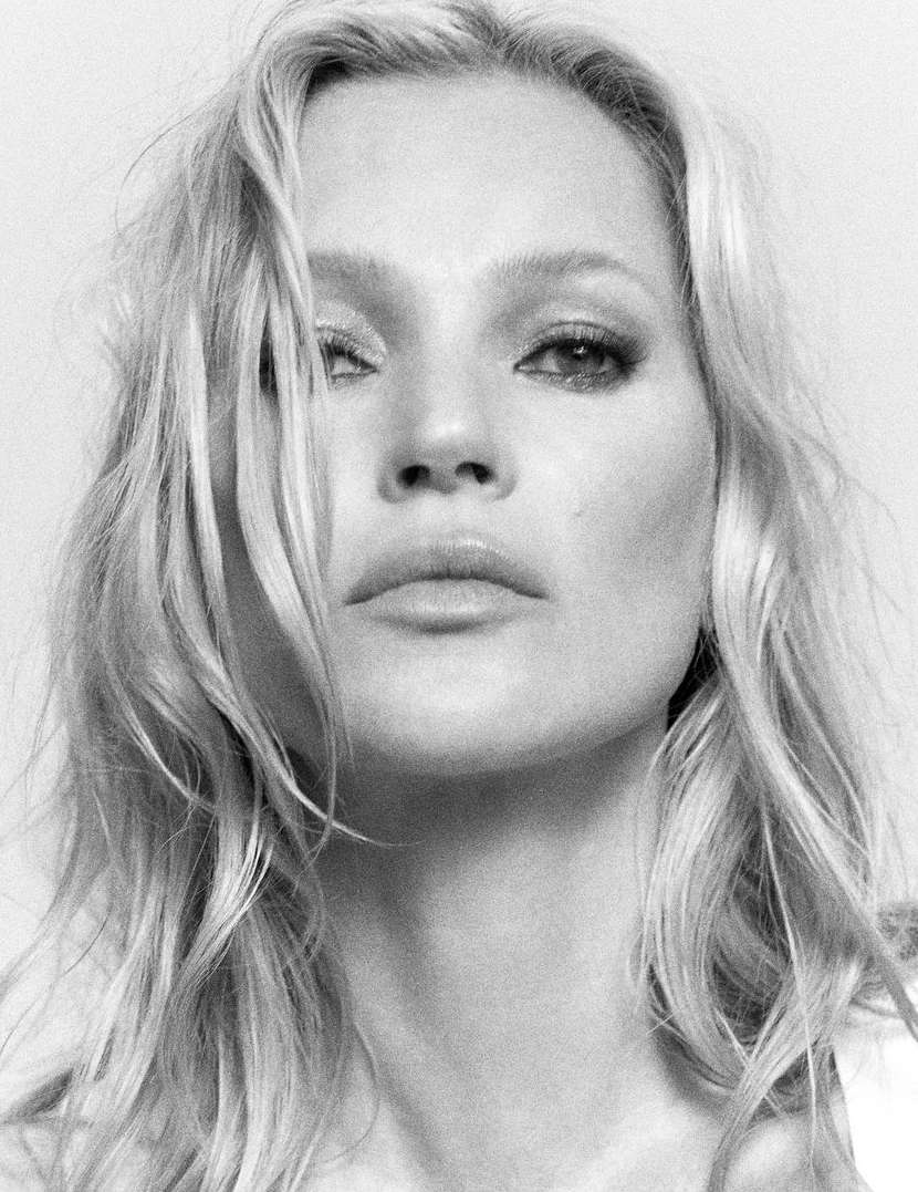 Close-up monochrome portrait of a blonde woman with tousled hair, direct gaze, and soft neutral makeup against a plain background