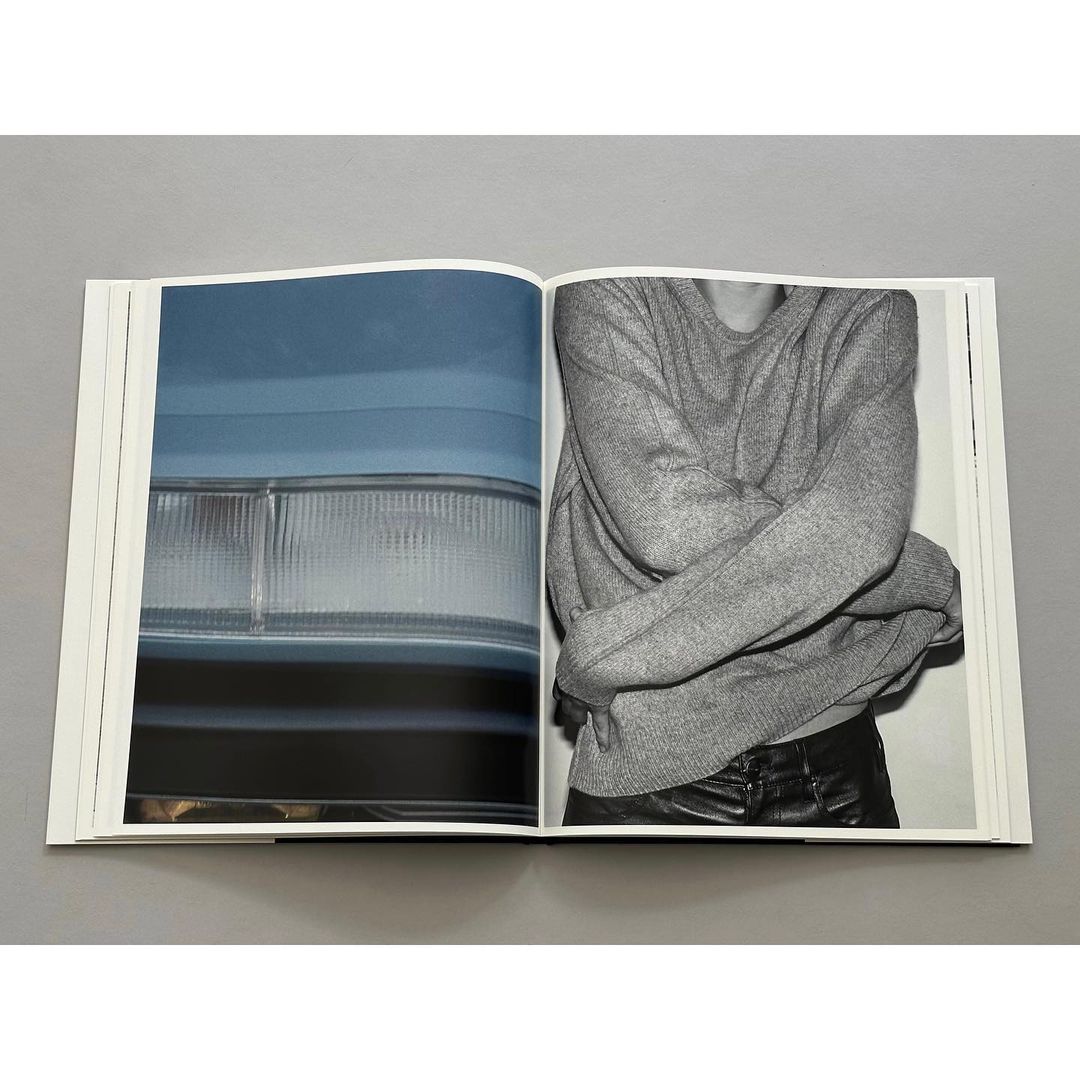 Open photography book featuring an abstract car headlight and a person with arms crossed wearing a grey sweater and black pants.