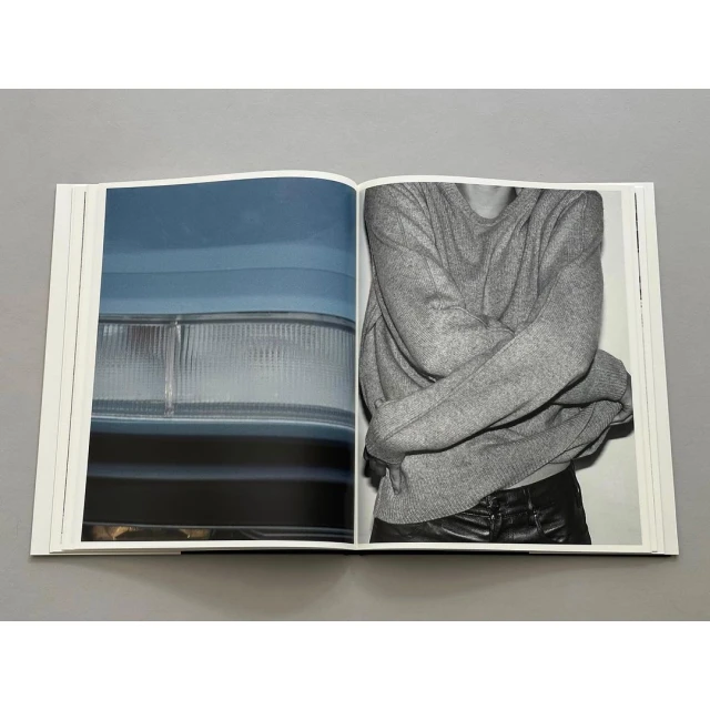 Open photography book featuring an abstract car headlight and a person with arms crossed wearing a grey sweater and black pants.