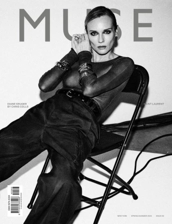 Black and white magazine cover featuring Diane Kruger posing in long sleeves and trousers, sitting on a chair in front of a white wall.