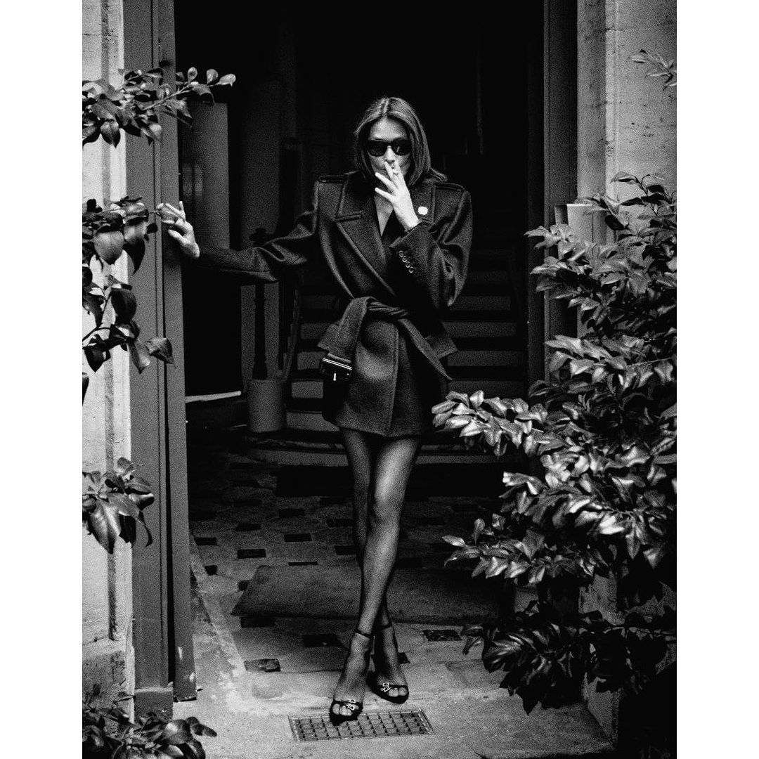 Monochrome fashion portrait of a woman in sunglasses and a belted coat posing in a doorway by Chris Colls
