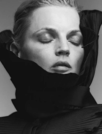 Close-up monochrome portrait of a woman with closed eyes wearing a structured black high-collar garment